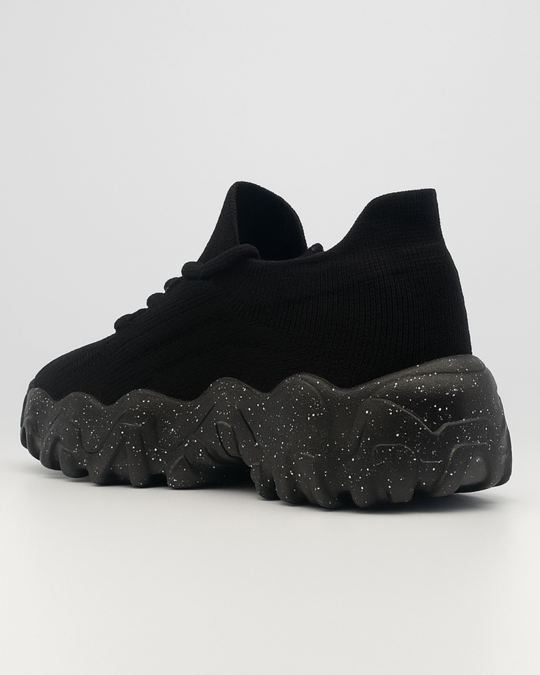 Three-quarter rear view of the black OrthoEase Luxe sneaker highlighting sole curve and heel shape.
