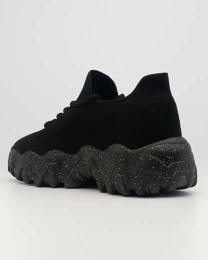 Three-quarter rear view of the black OrthoEase Luxe sneaker highlighting sole curve and heel shape.